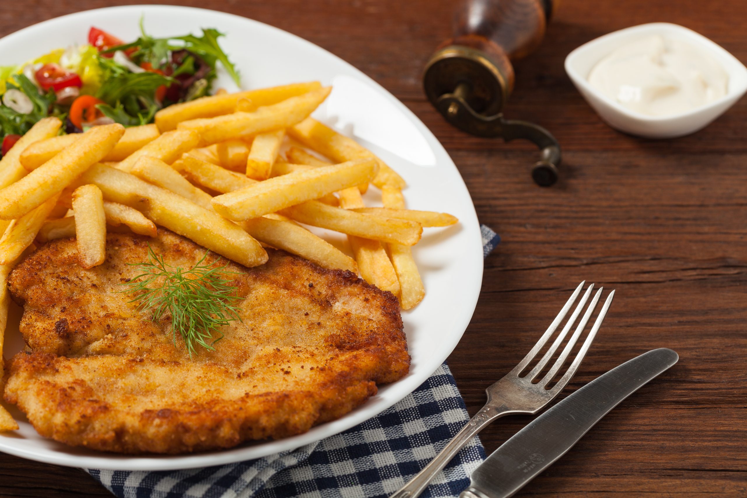 Chicken schnitzel, served with fries and salad. Chicken schnitzel, served with fries and salad. Natural wooden background. Front view.